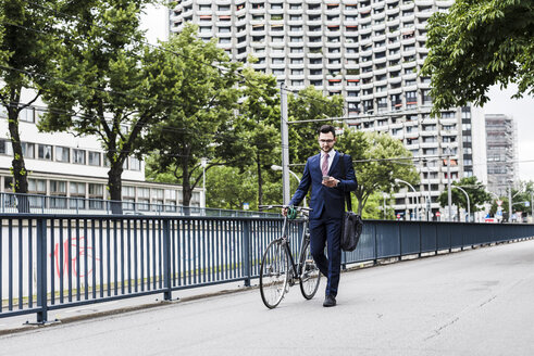Geschäftsmann mit Fahrrad in der Stadt, der sein Smartphone benutzt - UUF007993