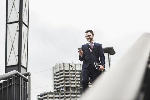 Junger Geschäftsmann steht am Geländer und benutzt ein Smartphone, lizenzfreies Stockfoto