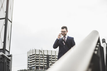 Young businessman standing at railing, using smart phone - UUF008011