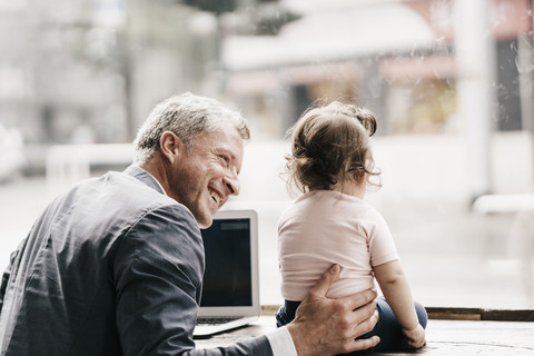 Geschäftsmann mit kleiner Tochter arbeitet am Laptop in einem Café, lizenzfreies Stockfoto