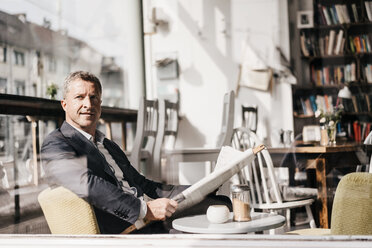 Businessman sitting in a cafe reading newspaper - KNSF000013