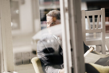 Businessman sitting in a cafe reading newspaper - KNSF000015