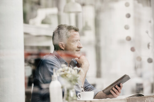 Älterer Mann sitzt im Café und liest ein E-Book - KNSF000033