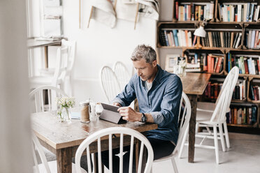 Mature man sitting in cafe reading at digital tablet - KNSF000040