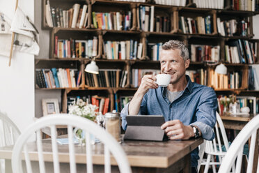 Mature man sitting in cafe with digital tablet, drinking coffee - KNSF000042