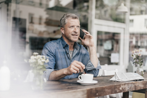 Älterer Mann sitzt im Café und telefoniert, lizenzfreies Stockfoto