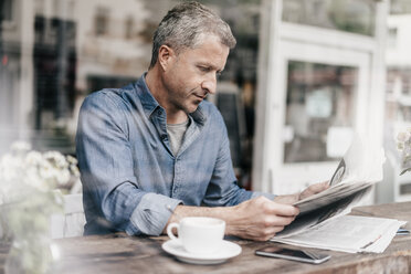 Mature man sitting in cafe reading newspaper - KNSF000053