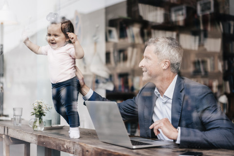 Geschäftsmann mit kleiner Tochter arbeitet am Laptop in einem Café, lizenzfreies Stockfoto