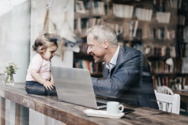 Businessman with little daughter working on laptop in cafe - KNSF000076