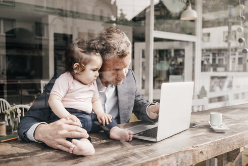 Geschäftsmann mit kleiner Tochter arbeitet am Laptop in einem Café - KNSF000077