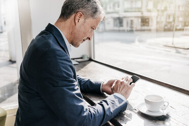 Businessman in cafe using smart phone - KNSF000090