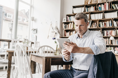 Geschäftsmann sitzt in einem Café und benutzt ein digitales Tablet, lizenzfreies Stockfoto