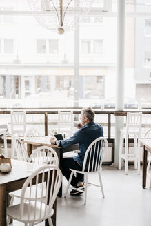 Älterer Mann mit digitalem Tablet trinkt Kaffee in einem Cafe - KNSF000102