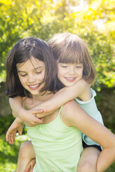 Girl giving her little sister a piggyback ride in the garden - LVF005114