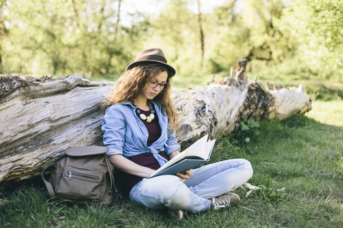 Frau sitzt auf einer Wiese und liest ein Buch, lizenzfreies Stockfoto