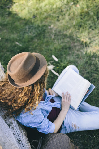 Frau sitzt auf einer Wiese und liest ein Buch, lizenzfreies Stockfoto