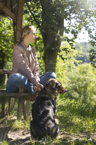 Junge Frau sitzt auf einer Holzbank und entspannt sich mit ihrem Hund, lizenzfreies Stockfoto