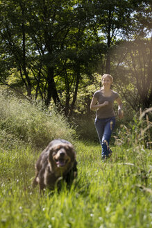 Junge Frau läuft ihrem Hund auf einer Wiese hinterher - MIDF000744