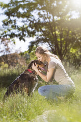 Junge Frau küsst ihren Mischlingshund auf einer Wiese - MIDF000749
