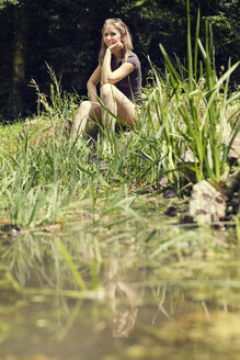 Smiling woman relaxing at water's edge - MIDF000754