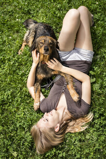 Junge Frau entspannt sich mit ihrem Hund auf einer Wiese - MIDF000758