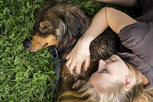 Junge Frau entspannt sich mit ihrem Hund auf einer Wiese - MIDF000759