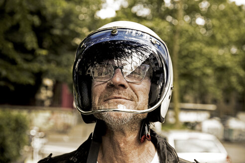 Portrait of smiling biker looking through vizor of his motorcycle helmet - FMKF002750