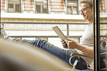 Man sitting on balcony using digital tablet - FMKF002751