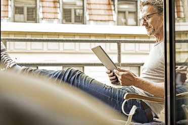 Mann sitzt auf einem Balkon und benutzt ein digitales Tablet - FMKF002751