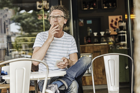 Smoking man sitting in front of a coffee shop stock photo