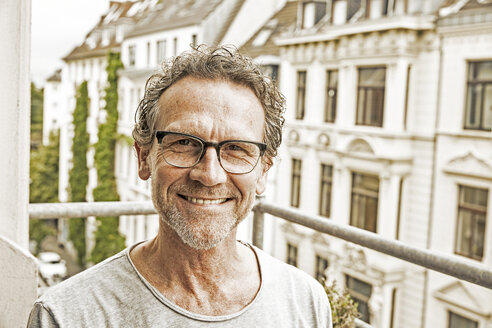 Portrait of happy man wearing glasses on his balcony - FMKF002754