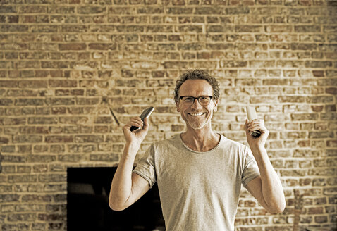 Portrait of happy man holding remote control - FMKF002761