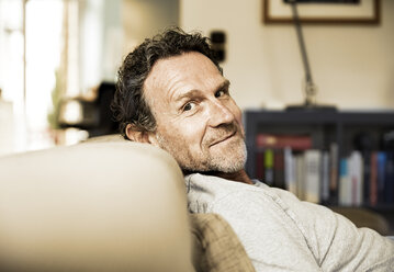 Portrait of smiling man with stubble relaxing on the couch - FMKF002766