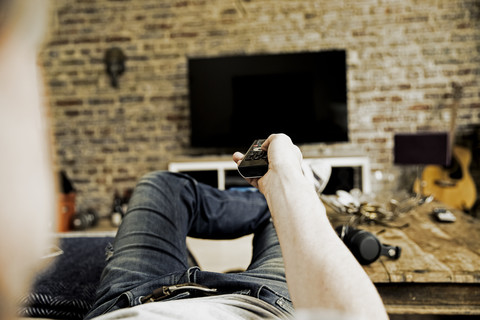 Mann auf der Couch liegend mit Fernbedienung, Teilansicht, lizenzfreies Stockfoto