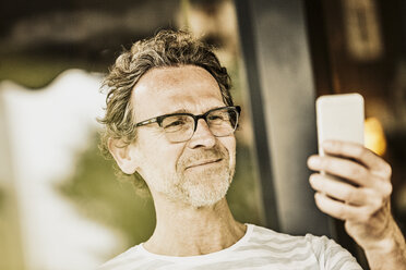 Porträt eines lächelnden Mannes mit Bartstoppeln, der ein Selfie mit seinem Smartphone macht - FMKF002768