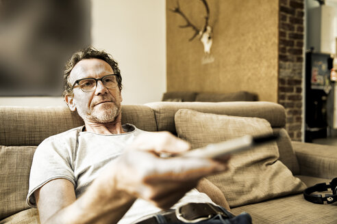 Portrait of man lying on the couch using remote control - FMKF002769