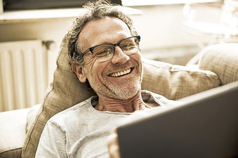 Portrait of laughing man lying on the couch using tablet stock photo