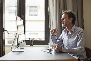 Geschäftsmann sitzt am Schreibtisch und schaut auf den Computer - FMKF002771