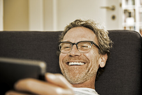 Portrait of laughing man lying on the couch using tablet - FMKF002772