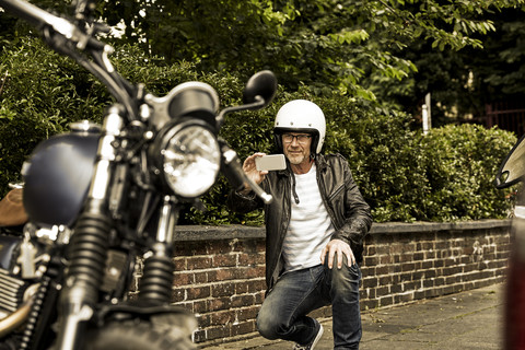 Smiling man with motorcycle helmet taking photo of his motorbike stock photo