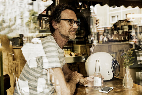 Man sitting behind windowpane of a coffee shop - FMKF002776