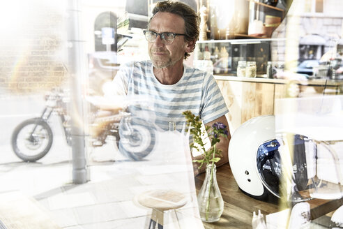 Man sitting behind windowpane of a coffee shop - FMKF002777