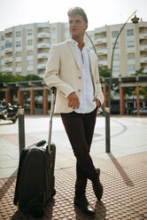 Young man with suitcase looking around - KIJF000524