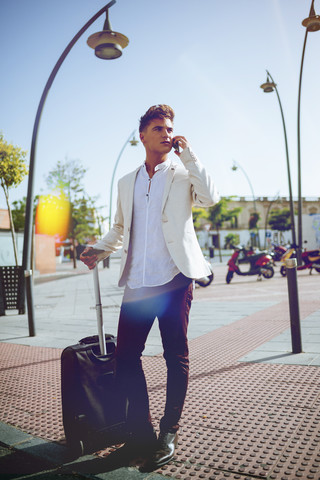 Junger Mann mit Koffer am Handy, lizenzfreies Stockfoto