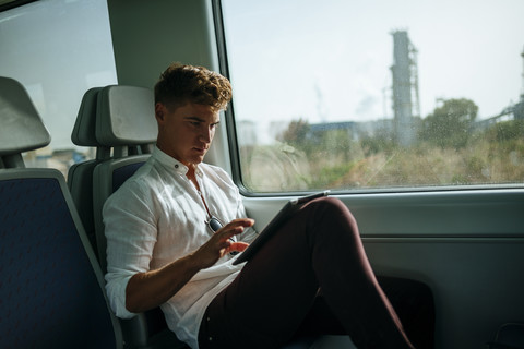 Junger Mann benutzt ein Tablet in einem Zug, lizenzfreies Stockfoto