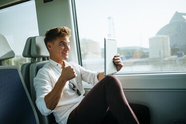 Junger Mann macht ein Selfie mit einem Tablet in einem Zug - KIJF000544