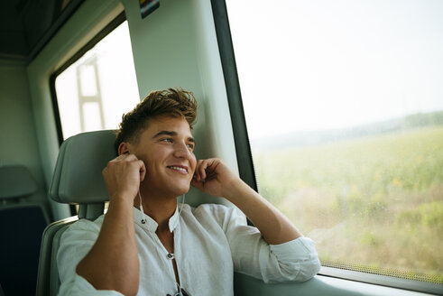 Junger Mann hört Musik und lächelt in einem Zug - KIJF000548