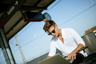 Young man using a laptop at station platform - KIJF000557