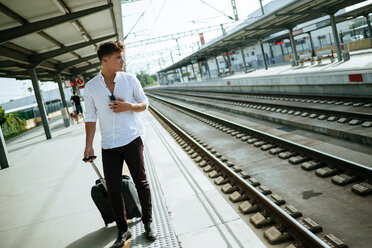 Young man with suitcase waiting at station platform - KIJF000561