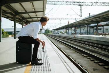 Young man with suitcase waiting at station platform - KIJF000563